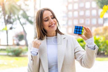 Junge hübsche Frau hält einen dreidimensionalen Puzzlewürfel im Freien und feiert einen Sieg
