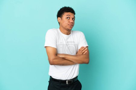 Junger afrikanisch-amerikanischer Mann isoliert auf blauem Hintergrund und macht eine Geste der Zweifel, während er die Schultern hebt
