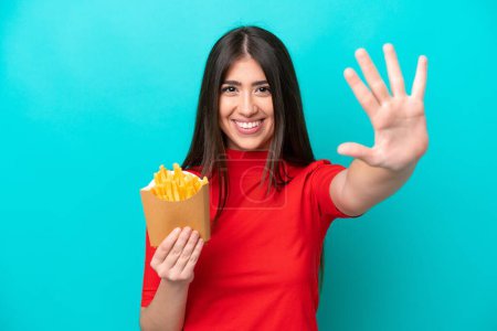 Photo for Young caucasian woman catching french fries isolated on blue background counting five with fingers - Royalty Free Image