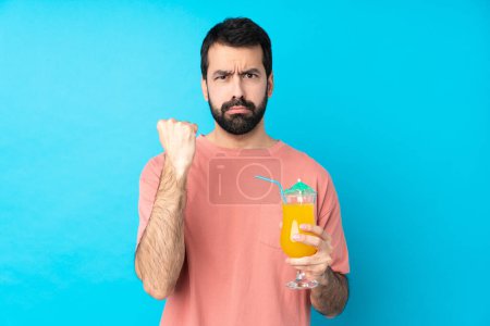 Téléchargez les photos : Jeune homme tenant un cocktail sur fond bleu isolé avec un geste de colère - en image libre de droit