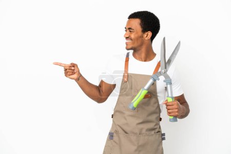 Photo for African American gardener man holding pruning shears over isolated white background pointing finger to the side and presenting a product - Royalty Free Image