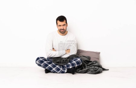 Foto de Hombre caucásico en pijama sentado en el suelo en el interior con expresión infeliz - Imagen libre de derechos
