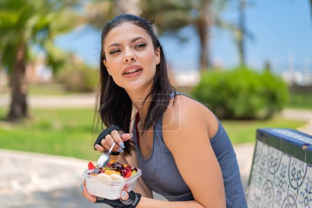 Photo for Young pretty sport woman holding a bowl of fruit at outdoors - Royalty Free Image