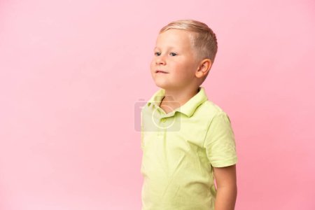 Foto de Pequeño chico ruso aislado sobre fondo rosa mirando hacia arriba mientras sonríe - Imagen libre de derechos
