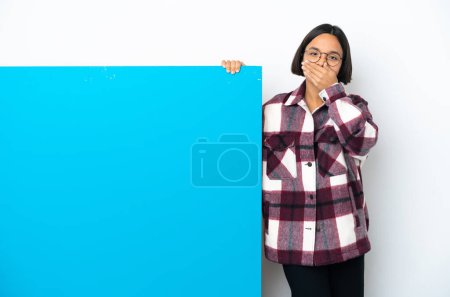 Foto de Mujer joven de raza mixta con un gran cartel azul aislado sobre fondo blanco que cubre la boca con las manos - Imagen libre de derechos