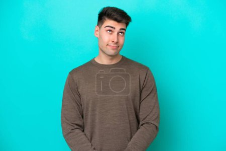 Photo for Young caucasian man isolated on blue background having doubts while looking up - Royalty Free Image