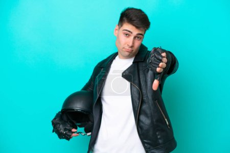 Foto de Joven hombre caucásico con casco de moto aislado sobre fondo azul mostrando el pulgar hacia abajo con expresión negativa - Imagen libre de derechos