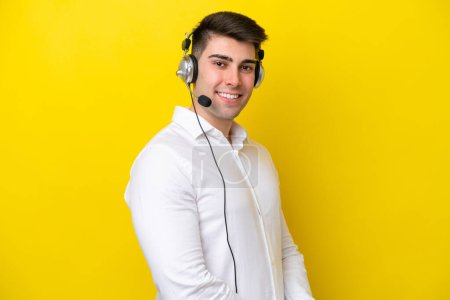 Photo for Telemarketer caucasian man working with a headset isolated on yellow background with arms crossed and looking forward - Royalty Free Image