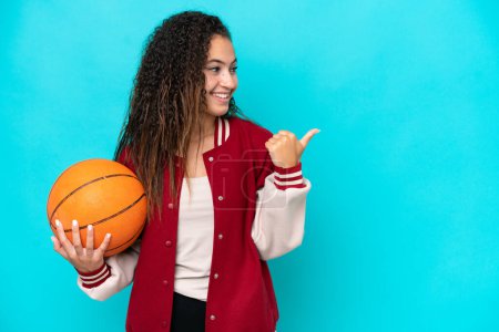 Téléchargez les photos : Joueuse arabe de basket femme isolée sur fond bleu pointant vers le côté pour présenter un produit - en image libre de droit