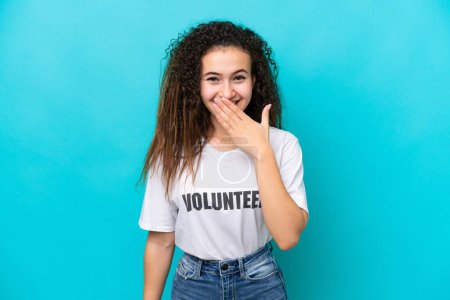 Junge arabische Freiwillige Frau isoliert auf blauem Hintergrund glücklich und lächelnd Mund mit der Hand bedecken