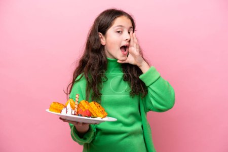 Photo for Little caucasian girl holding waffles isolated on pink background shouting with mouth wide open - Royalty Free Image
