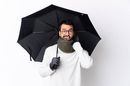 Téléchargez les photos : Homme beau caucasien avec barbe tenant un parapluie sur mur blanc isolé ayant des doutes - en image libre de droit