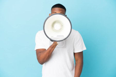 Photo for Young latin man isolated on blue background shouting through a megaphone to announce something - Royalty Free Image