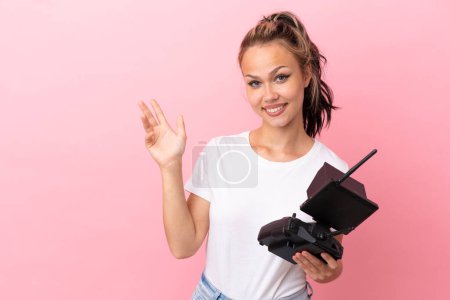 Adolescente rusa chica sosteniendo un teledirigido drone aislado sobre fondo rosa extendiendo las manos a un lado para invitar a venir