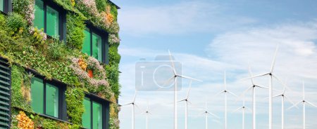 Außenseite eines grünen, nachhaltigen Gebäudes mit blühenden senkrecht hängenden Pflanzen vor Windkraftanlagen