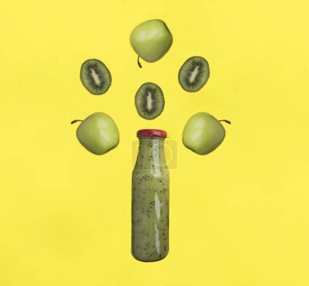Foto de Batido con manzana verde y kiwi en la botella de vidrio sobre el fondo amarillo. Copiar espacio. Primer plano. - Imagen libre de derechos
