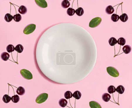 Téléchargez les photos : Empty white plate for text, cherries and mint on the pink background. Copy space. Top view. - en image libre de droit