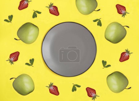 Téléchargez les photos : Assiette vide grise pour texte, pomme et fraise sur fond jaune. Vue de dessus. Espace de copie. - en image libre de droit