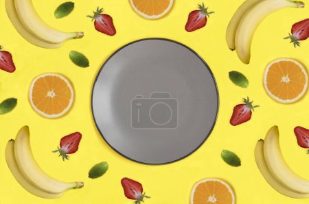 Téléchargez les photos : Empty gray plate for text, fruit and berry on the yellow background. Copy space. Top view. - en image libre de droit