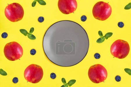Empty gray plate for text, red apple and blueberry on the yellow background. Top view. Copy space.