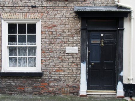 vue de face d'une ancienne petite maison en brique anglaise en terrasses avec porte peinte en noir et fenêtre blanche