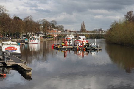 Photo for Chester. Cheshire, United Kingdom - 20 March 2024 : View of the river Dee in Chester with trip boats moored on the riverbank and the queens park suspension bridge - Royalty Free Image