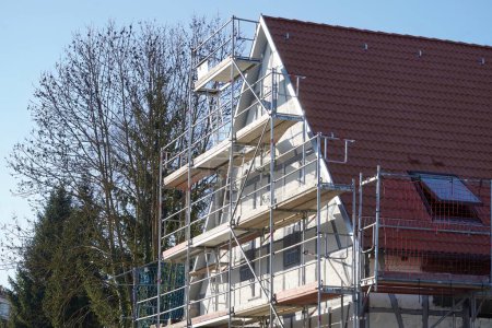 Téléchargez les photos : House renovation - energetic renovation. The old house is completely scaffolded on the front and the new color is already shining brightly in the winter sun. - en image libre de droit