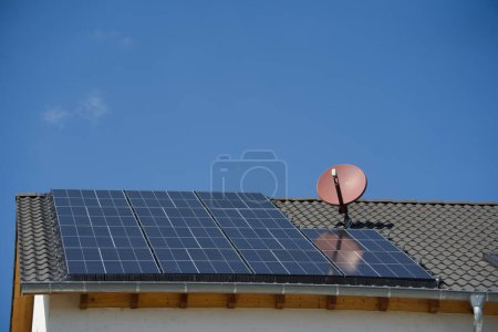 Foto de Los módulos solares sobre el techo plano de la casa brillan bajo el sol brillante del mediodía. Una nueva paloma disuasoria se ha instalado en la alcantarilla - Imagen libre de derechos