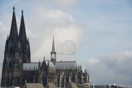 The Cologne Cathedral with its high towers in the overall view. The cathedral towers over all the residential roofs in the neighborhood. But compared to the gigantic mountains of clouds in the sky, the Gothic structure seems almost small