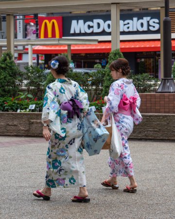 Photo for Japanese women dressed in traditional kimonos pass McDonalds in Tokyo. - Royalty Free Image