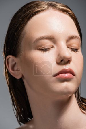 Porträt einer jungen Frau mit feuchter Haut, die die Augen auf Grau schließt 