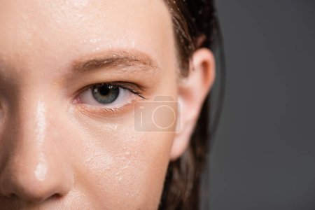 Ausgeschnittene Ansicht einer Frau mit nasser Haut und verschwommenem Haar, die isoliert auf grau schaut 