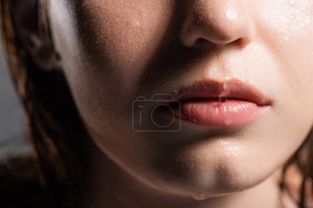 Vista recortada de gotas de agua en los labios de una joven aislada en gris 