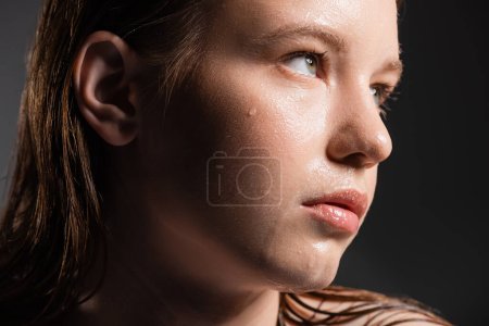 Close up view of fair haired woman with water on face looking away on grey background 