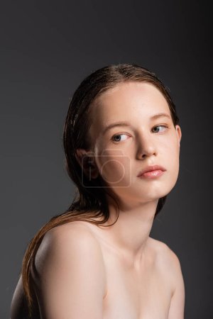 Junge Frau mit nassen Haaren und nackten Schultern schaut vereinzelt auf grau 