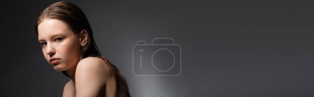 Young model with wet face and shoulders looking at camera on grey background, banner 