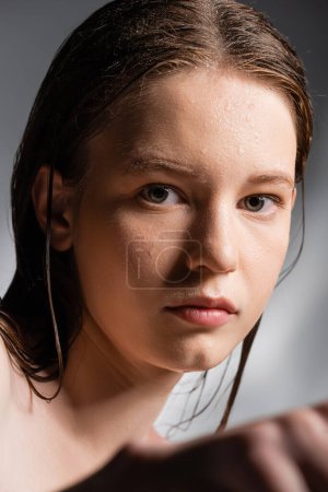 Retrato de mujer joven con la piel mojada en la cara mirando a la cámara sobre fondo gris 