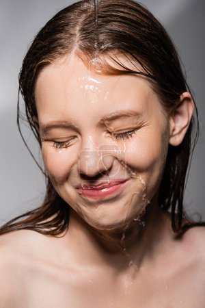 Smiling woman with water on face closing eyes on grey background 