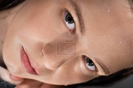 Nahaufnahme einer jungen Frau mit nassem Gesicht, die auf einem Spiegel liegt 