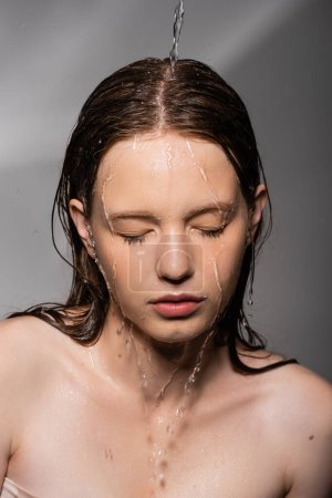 Wasser ergießt sich auf Haare und Gesicht des jungen Models auf grauem Hintergrund 