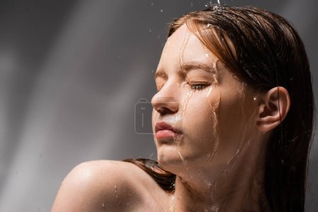Téléchargez les photos : Jolie jeune femme avec épaule nue debout sous l'eau sur fond gris abstrait - en image libre de droit