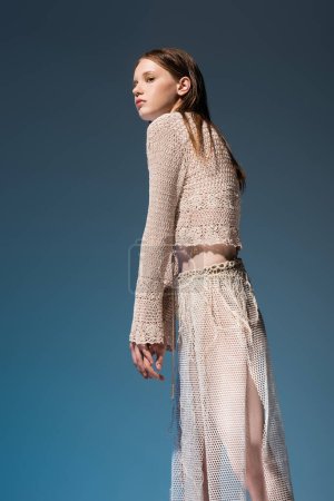 woman in fishnet skirt and cardigan looking away on gradient blue background 