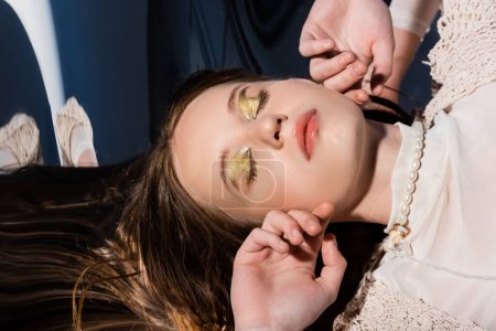 Top view of woman with golden makeup lying on reflective surface on abstract background 