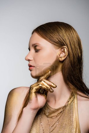 Pretty young model with golden paint on hand and chin posing isolated on grey 