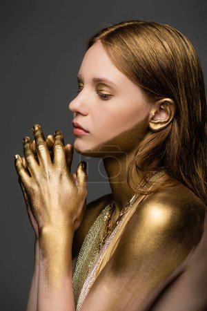 Woman with golden paint on skin and hair standing isolated on grey 