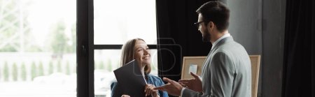 Smiling woman holding resume while businessman talking during job interview in office, banner 