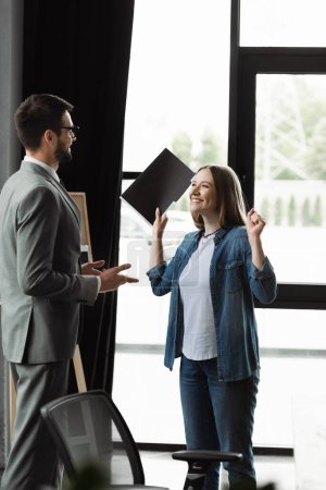 Mujer emocionada sosteniendo curriculum vitae cerca de hombre de negocios durante la entrevista de trabajo en la oficina 