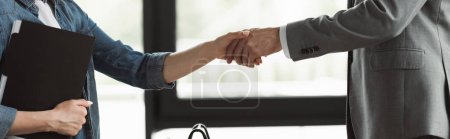 Cropped view of woman with resume shaking hand of businessman in suit in office, banner 