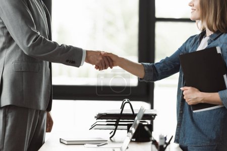 Cropped view of smiling woman with resume shaking hand of businessman during job interview in office