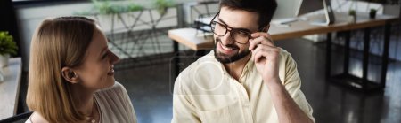 Smiling manager touching eyeglasses while talking to intern in office, banner 